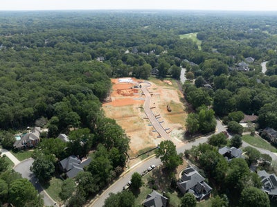 Aerial view of a residential construction site with cleared lots and new roads surrounded by wooded neighborhood homes.