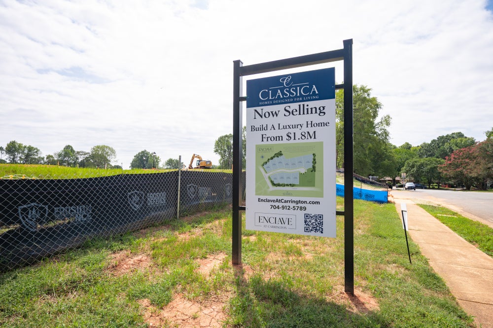 Classica Homes new development sign for Enclave at Carrington, advertising luxury homes from $1.8M, with active construction site behind fencing.