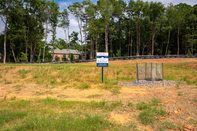 Vacant residential lot for sale with cleared land, erosion fencing, and wooded tree line in background