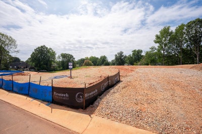 Cleared residential building lot with gravel, dirt, and erosion control fencing along the curb