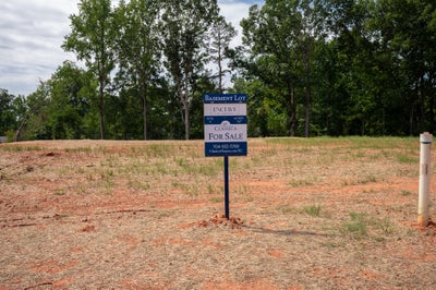 Vacant basement lot for sale at Enclave community with cleared red clay ground and trees in background